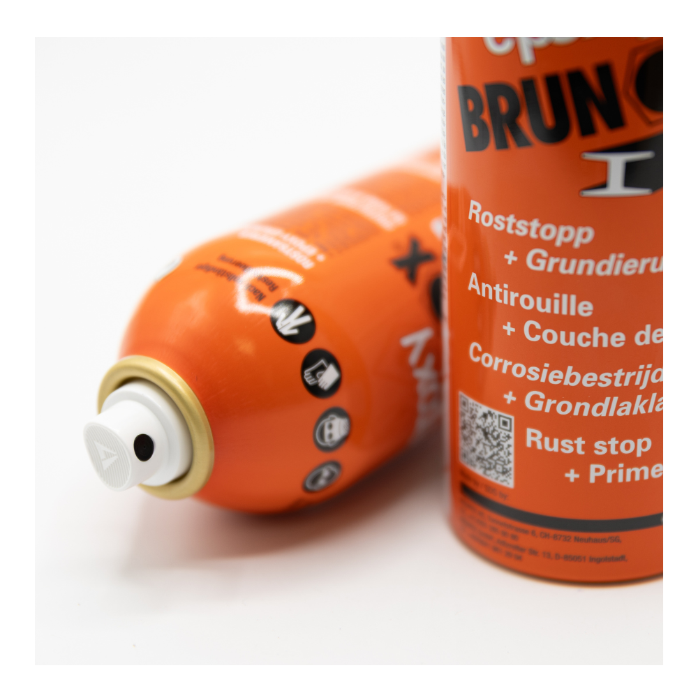 Twee oranje BRUNOX‑spuitbussen, één rechtop en één liggend, met zichtbare nozzle en meertalige roeststop‑primerinformatie.